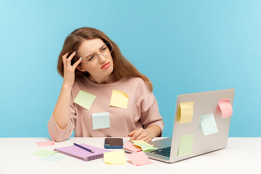 Pensativa molesta mujer empleada en gafas nerd sentado en la oficina del lugar de trabajo, todo cubierto con notas adhesivas photo