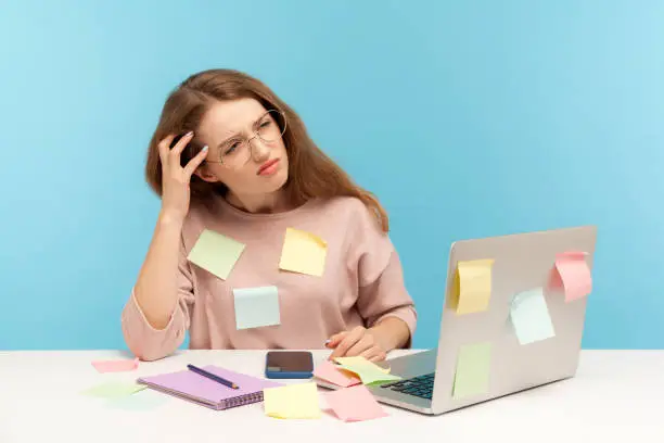 Photo of Pensive upset woman employee in nerd eyeglasses sitting at workplace office, all covered with sticky notes