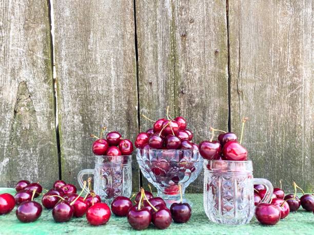 Large ripe red cherries in glass containers on a background of an abstract wooden surface.
