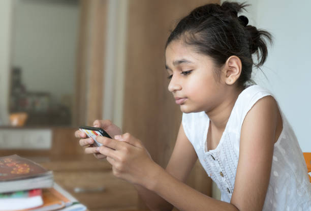 istock Asian/Indian little girl busy in using mobile phone after study. 1258832662