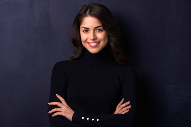 istock Attractive young woman looking at camera and smiling while standing at dark background 1258838932