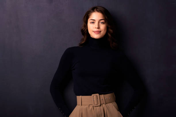 istock Attractive young woman looking at camera and smiling while standing at dark background 1258838933