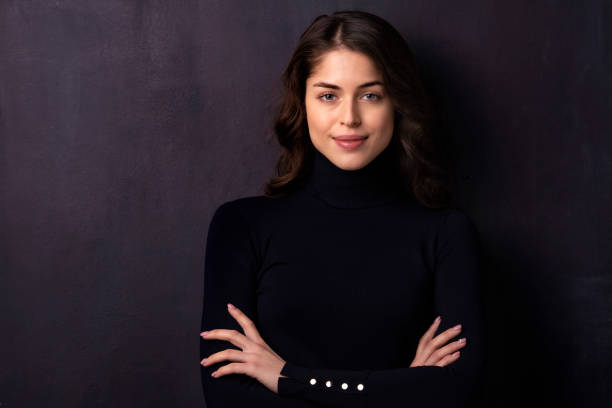 istock Attractive young woman looking at camera and smiling while standing at dark background 1258838934