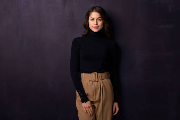 istock Attractive young woman looking at camera and smiling while standing at dark background 1258838938