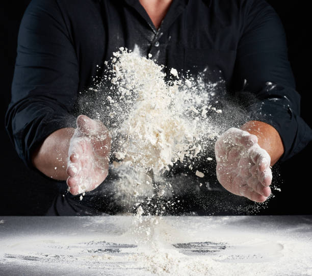 istock chef in black uniform sprinkles white wheat flour in different directions, product scatters dust 1258843152