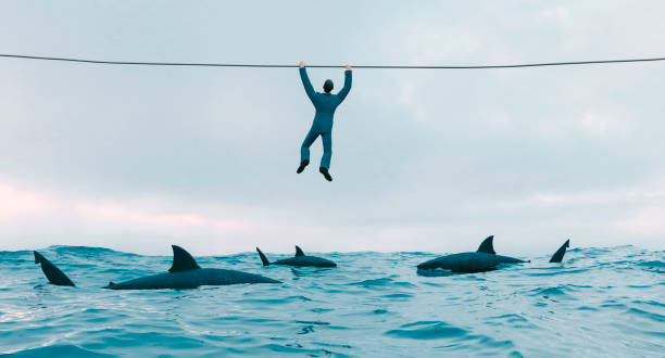 istock Surrounded by sharks looking for a prey man holds on to wire above water 1258859863