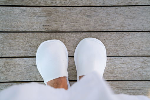 Woman staying in white slippers on wooden floor in hotel terrace. Top View . High quality photo