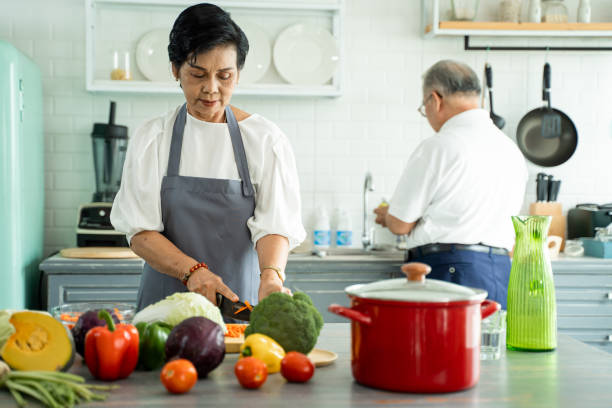 istock Elderly Asian woman cooking and cutting ingredients on table while preparing lunch with husband in cozy kitchen at home. Senior Asian couple cooking together 1258968733