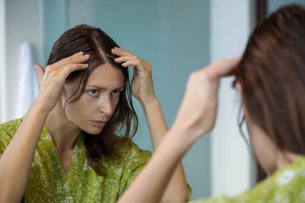 porträt einer schönen jungen frau, die ihre kopfhaut und haare vor dem spiegel, haarwurzeln, farbe, grauehaare, haarausfall oder trockene kopfhaut problem untersucht - graues haar stock-fotos und bilder