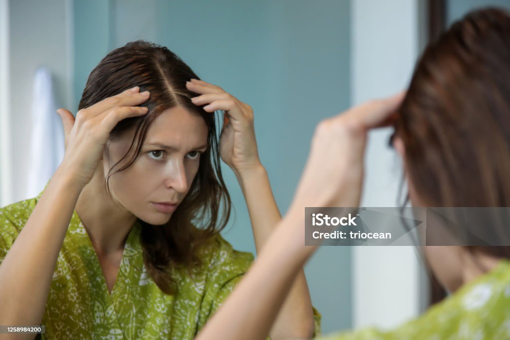 Portrait of a beautiful young woman examining her scalp and hair in front of the mirror, hair roots, color, grey hair, hair loss or dry scalp problem Gray Hair Stock Photo
