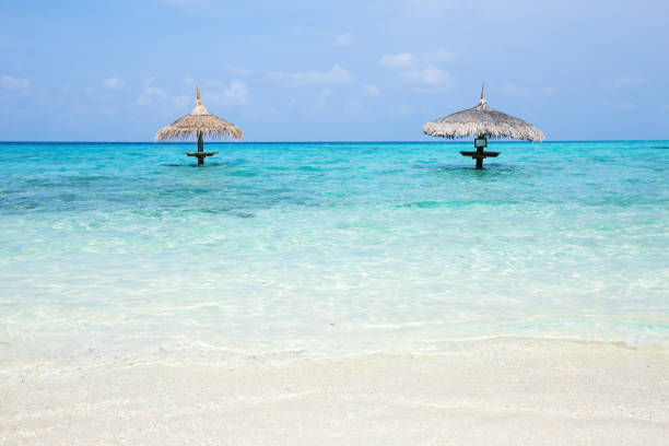 Two thatched sunshade umbrellas Two thatched sunshade umbrellas at crystal turquoise sea water, nobody, travel destination card with copy space water bungalow maldives stock pictures, royalty-free photos & images