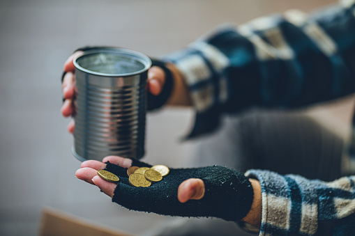 Hands of homeless person holding money can and coins