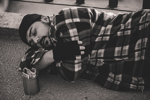 Poor homeless man sleeping on the ground with money tin near him