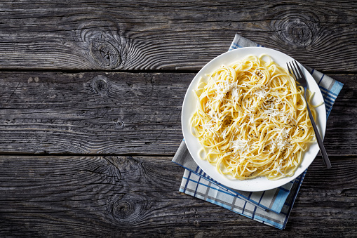 creamy spaghetti with cheese and dusted with ground black pepper on a white plate on an old  wooden table, cacio e pepe, Italian cuisine, view from above, flatlay, empty space left