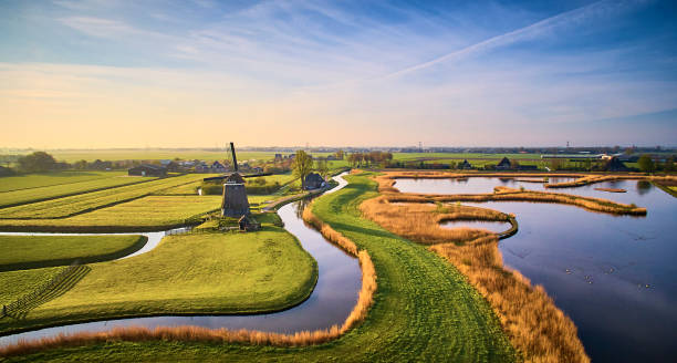 Dutch landscape during sunrise Dutch landscape during sunrise. The picture is made from above. In the middle of the picture is a windmill. There are different canals and between the parts of water are pieces of land consisting of grass. netherlands aerial stock pictures, royalty-free photos & images