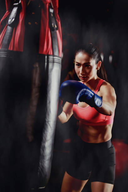 asiático mujer entrenamiento con saco de boxeo - boxing womens fotografías e imágenes de stock