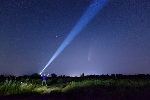 Man with flashlight against amazing night starry sky with comet