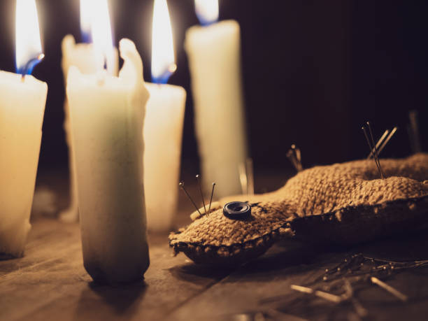 istock Rag doll voodoo pierced with needles, lying on a wooden table surrounded by burning candles, close-up. The concept of divination, rite, ritual and black magic. Harming people with a voodoo doll 1259042000
