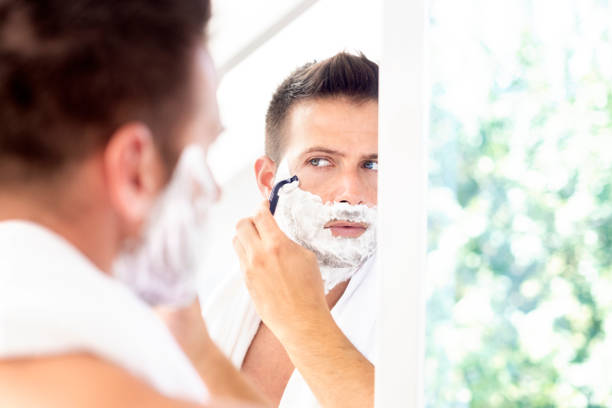 istock Handsome man shaving his beard while standing in front of a mirror 1259089196