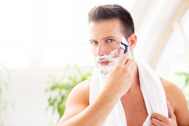 istock Handsome man shaving his beard while standing in front of a mirror 1259089197