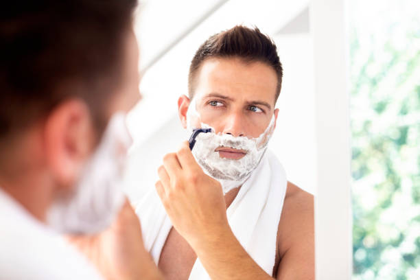 istock Handsome man shaving his beard while standing in front of a mirror 1259089200