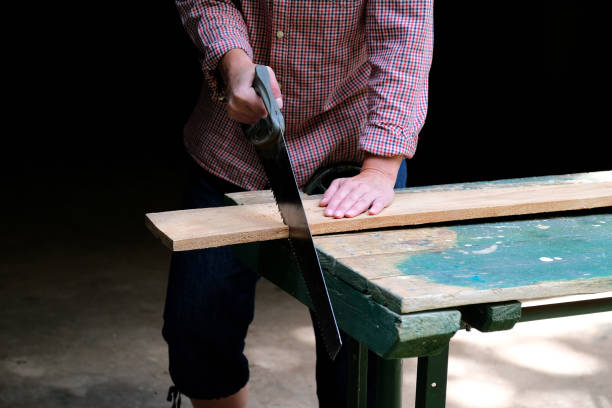 istock Carpenter woman with handsaw cutting wooden board in workshop. Carpentry, construction, woodworking concept. 1259104229