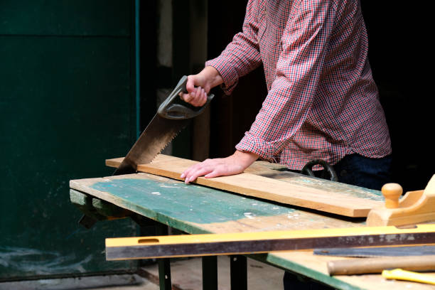 istock Craftswoman cutting plank with handsaw in workshop. Carpentry, construction, woodworking concept. 1259104234
