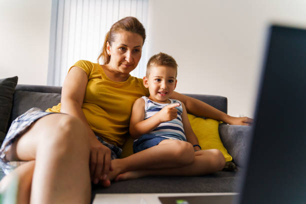istock Small caucasian boy pointing finger to the screen shoving his mother while watching online content on laptop - Little child son sitting by his mom at home in front of the computer - childhood concept 1259110323