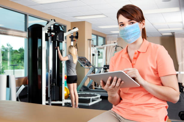 Female Physical Therapist Wearing Protective Mask Charting on Digital Tablet