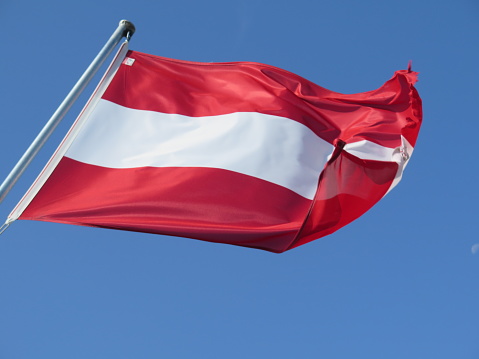 Flag of Austria waving in wind on a pole in front of blue sky