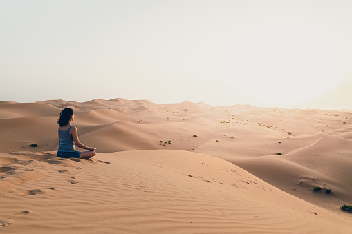 Young woman meditating in the desert, at the Wildlife resort during sunset
