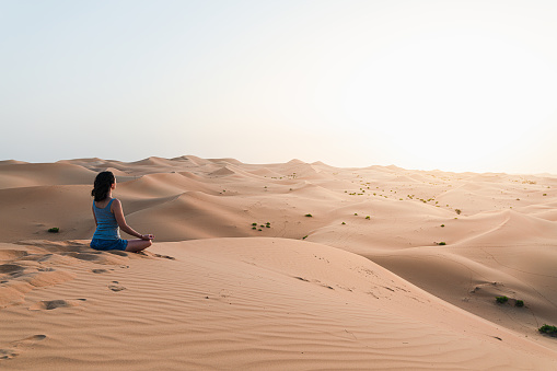 Young woman meditating in the desert, at the Wildlife resort during sunset