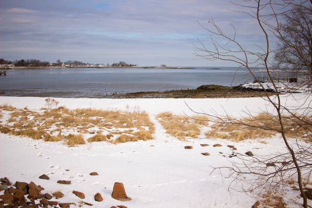 Low angle view of clear water of a tide pool and rippled sand on beach at Greenwich Point, Greenwich, CT, USA with sun bright in blue sky giving sun rays