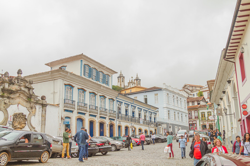 June 26, 2019 - Ouro Preto, Minas Gerais, Brazil: National and international tourists walking and enjoying a cloudy winter day at Town square in Our Preto's colonial City. Bright colored facades of traditional brazilian rural houses with typical wood commercial signs as Coffee Shops, Restaurants, Jewelry Shops, etc around the square.\n\nOuro Preto is a former colonial mining town in Minas Gerais, designated a World Heritage Site by UNESCO.\n\nFounded in latest 17th century, Ouro Preto means in english \