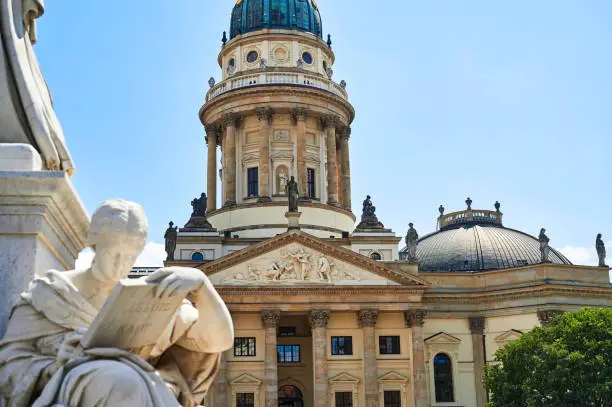 View to the German Cathedral and an unfocussed part of the Schiller Fountain in the foreground in downtown Berlin at the historic square Gendarmenmarkt.