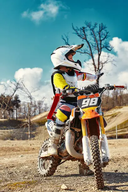 Photo of Portrait of boy dressed and equipped for motorbike racing sitting on motorcycle