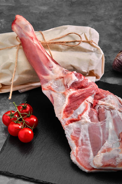 istock Raw lamb leg on marble cutting board. Dark background. Side view 1259150622