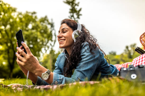 belle femme écoutant la musique sur son casque dans le parc - headphones relaxation outdoors caucasian photos et images de collection