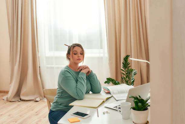 istock Online study. Young beautiful focused female student studying at home, sitting at her comfortable workplace at home office. Desk with laptop, handbook, notebook 1259160018