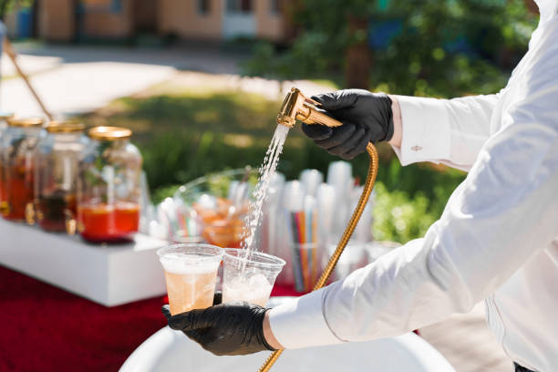 istock Waiter pours cider into plastic cups from bathroom faucet. Creative welcome drink zone. Bath with ice cubes, fruits, lemonades at hot summer day 1259177169