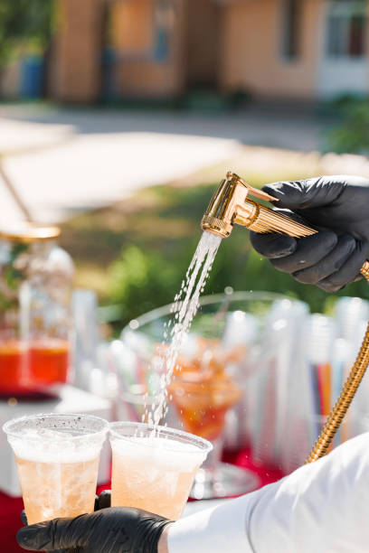 istock Waiter pours cider into plastic cups from bathroom faucet. Creative welcome drink zone. Bath with ice cubes, fruits, lemonades at hot summer day 1259177174