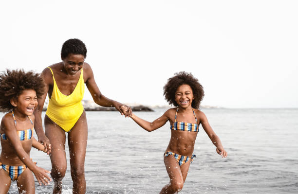 felice famiglia africana che corre in spiaggia durante le vacanze estive - persone afro-americane che si divertono in vacanza - i genitori amano e viaggiano concetto di stile di vita - child caribbean black latin american and hispanic ethnicity foto e immagini stock