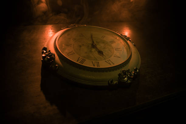 istock Time concept. Big vintage round clock on wooden table with abstract light. 1259212783