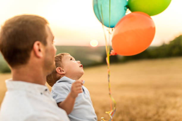 Happy smiling five years old boy with colorful balloons jumping outdoors on sunny day and clear blue sky