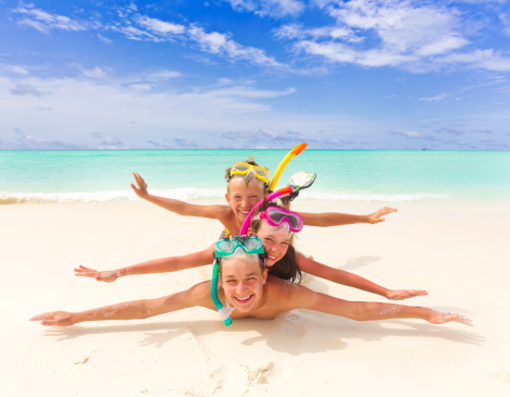 \tThree happy children with snorkels pretending to swim on sandy tropical beach, sea and blue sky background.