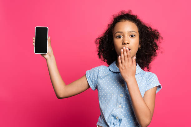 istock shocked curly african american kid presenting smartphone isolated on pink 1259227280