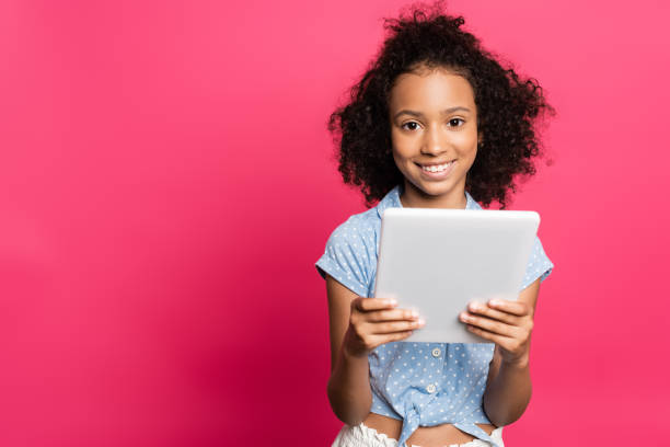 istock smiling cute curly african american kid using digital tablet isolated on pink 1259227283