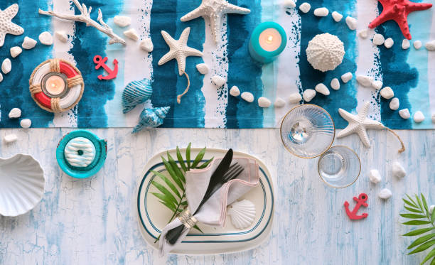 istock Contemporary Summer table setting with nautical sea decorations on blue and white stripy runner, classic blue white plates, utensils on white rustic table. Top view, casual modern lunch. 1259227850