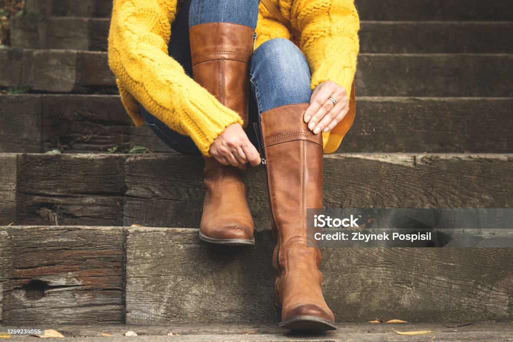 Woman fasten zipper on her leather boot Woman sitting on stairs and fasten zipper on her leather boots. Autumn fashion concept Boot Stock Photo
