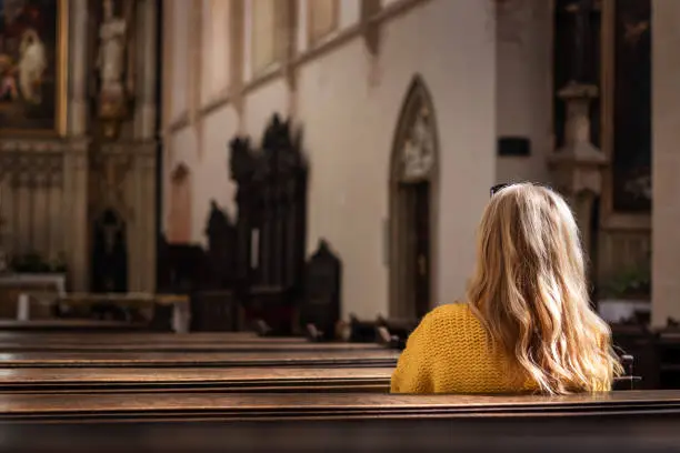 Woman sitting on pew and praying in empty church. Catholic religion at European culture. Faith and hope concept